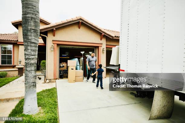 young son helping father move items from moving truck into new house - camión de las mudanzas fotografías e imágenes de stock