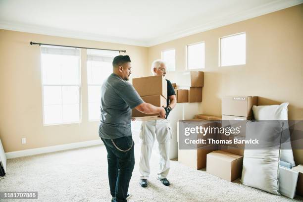 father in law and son in law moving boxes in living room on moving day - assisted living stock-fotos und bilder