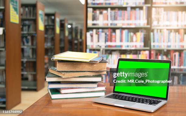 computer laptop with green screen and book stack in library room.education background concept - archive library stock-fotos und bilder