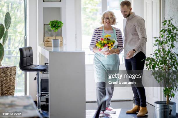 smiling senior woman with bunch of flowers received from young man - old woman young man stock pictures, royalty-free photos & images