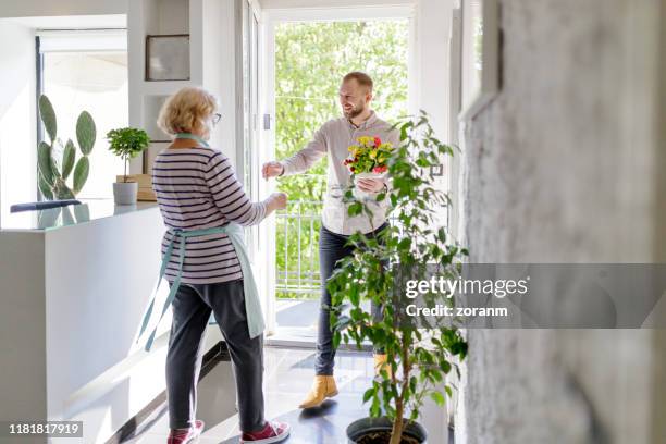 young man reaching for handshake with senior woman at the door - surprise guest stock pictures, royalty-free photos & images