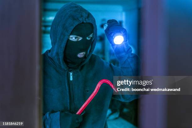 masked burglar with crowbar breaking and entering into a victim's home - einbruch stock-fotos und bilder