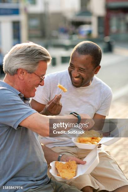 senior men smiling holding fish and chips - fish and chips stock pictures, royalty-free photos & images