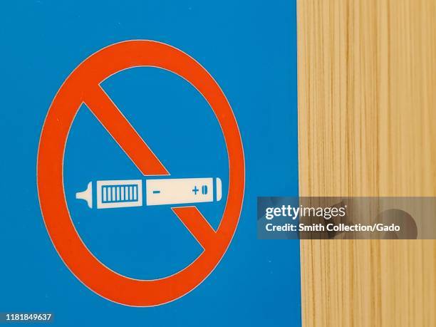 Close-up of No Vaping sign on light wooden wall surface, with stylized image of a vaping device or e-cigarette crossed out with a red circle, San...