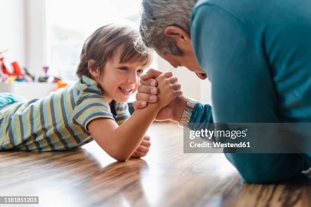 father and son lying on the floor at home arm wrestling - echar un pulso fotografías e imágenes de stock