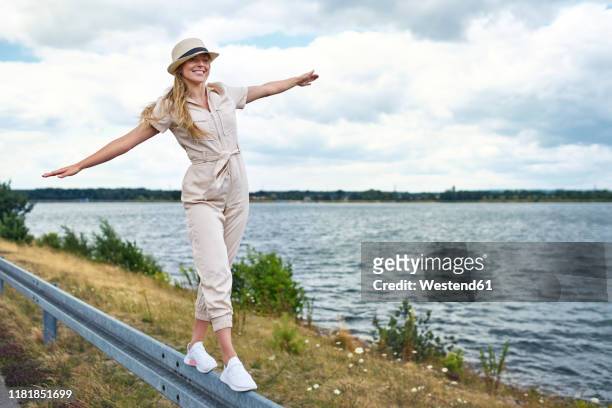 happy woman balancing on crash barrier at the lakeside - white jumpsuit stock pictures, royalty-free photos & images