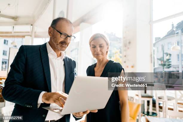 businessman and woman standing in coffee shop, using laptop - two executive man coffee shop stockfoto's en -beelden