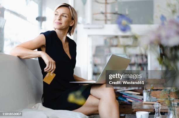 businesswoman making online payment, sitting in coffee shop, using laptop and credit card - business credit card stockfoto's en -beelden