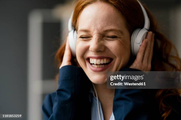 portrait of laughing redheaded businesswoman listening music with white headphones - persoon luisteren muziek oortjes stockfoto's en -beelden