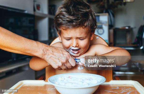 little boy eating yogurt at home, hand of woman on the spoon - angry parent mealtime stock pictures, royalty-free photos & images
