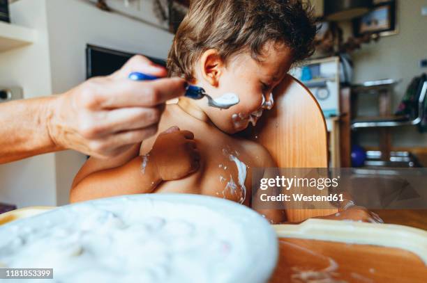 little boy eating yogurt at home, turning away his head - spoon in hand stock-fotos und bilder