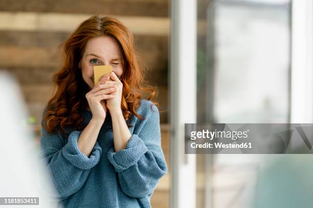 portrait of redheaded woman with credit card in a loft - winking stockfoto's en -beelden
