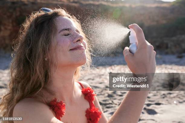 young woman applying suncream spray on the beach - summer skin stock pictures, royalty-free photos & images