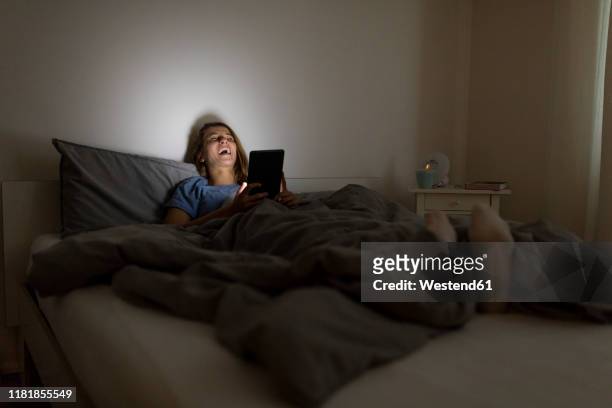 laughing young woman lying in bed at home at night using tablet - funny hobbies stock pictures, royalty-free photos & images