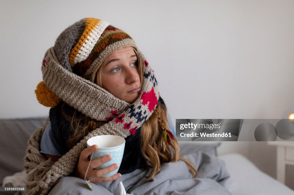 Ill young woman drinking tea in bed at home