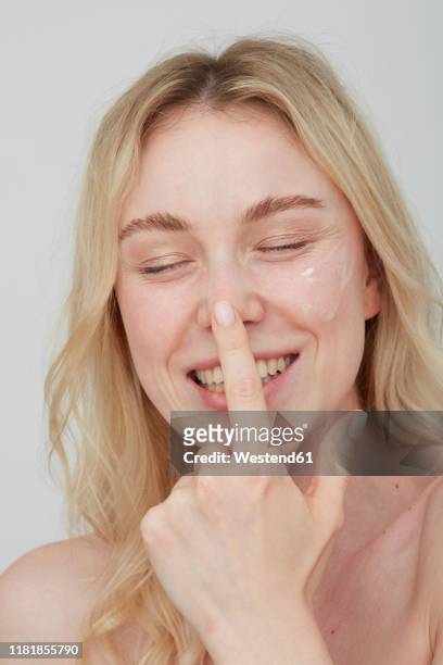 portrait of laughing young woman applying cream on her face - beauty studio moisturisers stock-fotos und bilder