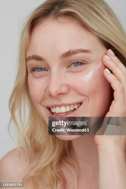 portrait of smiling young woman applying cream on her face - face cream stock pictures, royalty-free photos & images