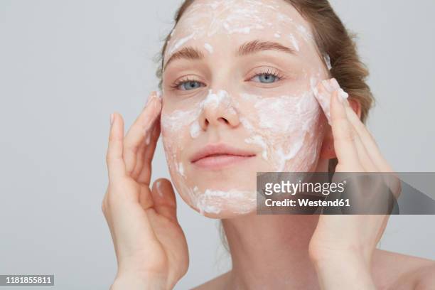 portrait of blond young woman applying cream on her face - mud mask photos et images de collection