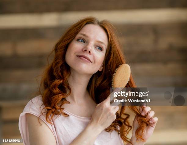 portrait of smiling redheaded woman brushing her hair - cepillar el cabello fotografías e imágenes de stock