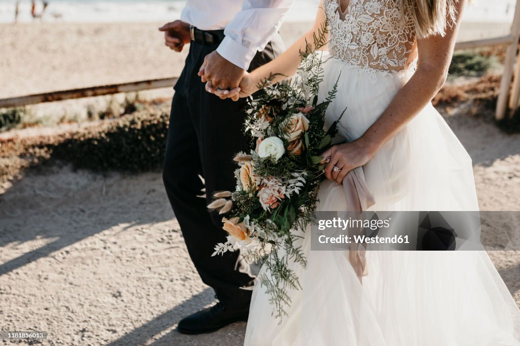 Close-up of bride and groom walking on path at the coast