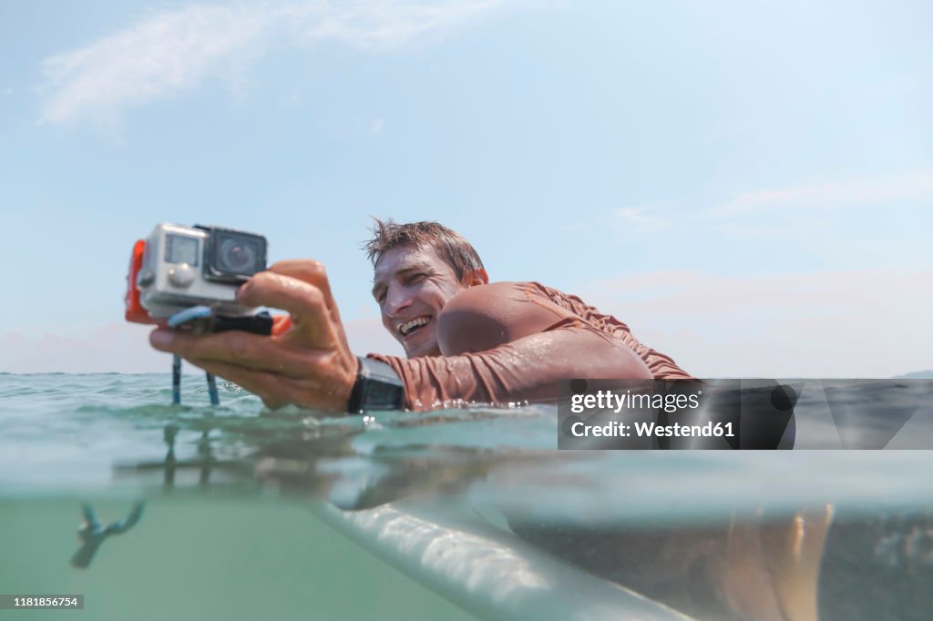 Surfer with action camera lying on surfboard