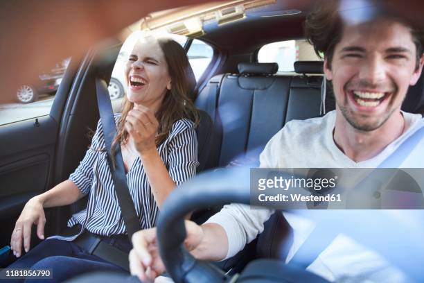 laughing couple in a car with man driving - freie fahrt stock-fotos und bilder