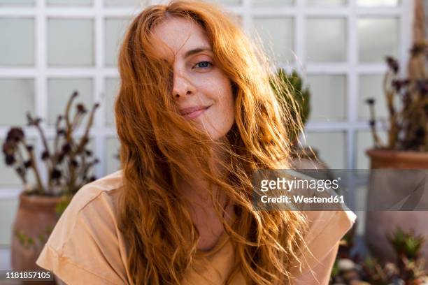 portrait of smiling redheaded young woman on terrace - haare stock-fotos und bilder