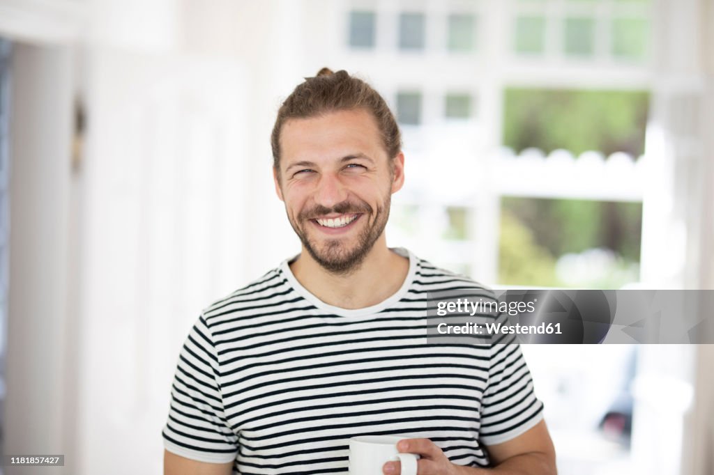 Portrait of smiling young man holding cup of coffee at home