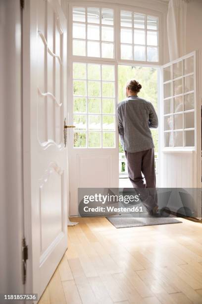 young man in pyjama standing at the terrace door at home - french doors stockfoto's en -beelden