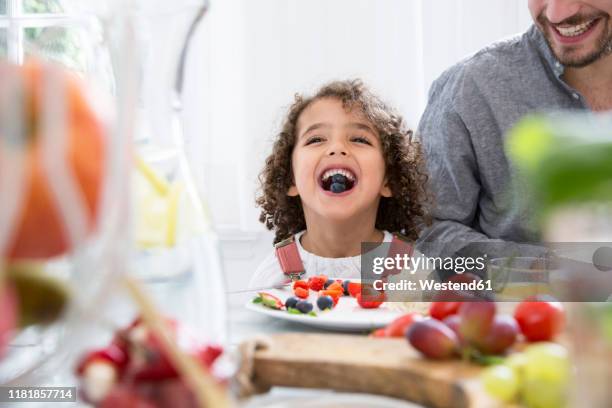 playful boy with his father eating blueberries at table - child eating a fruit stockfoto's en -beelden