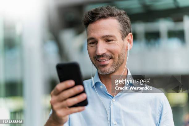 smiling businessman with earphones and cell phone in the city - powder blue shirt stock pictures, royalty-free photos & images