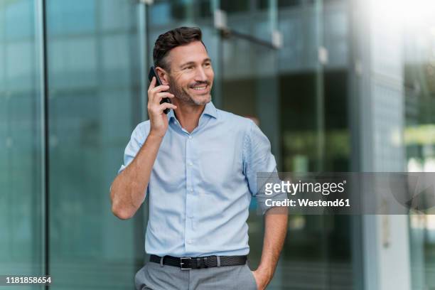 smiling businessman on cell phone in the city - rolling up sleeve stock-fotos und bilder