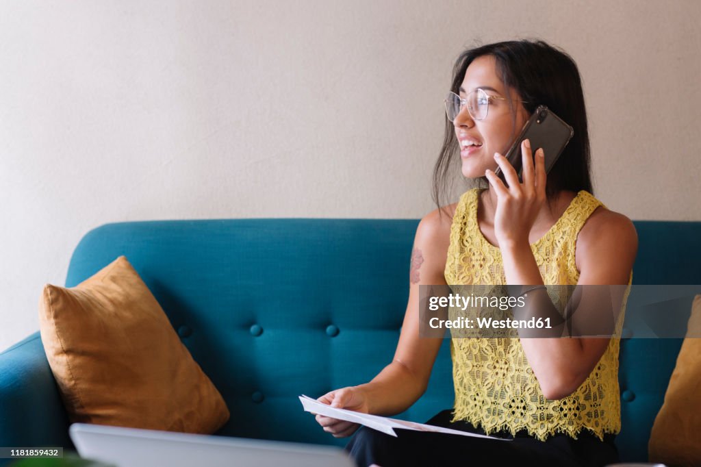 Smiling young woman sitting on couch talking on the phone