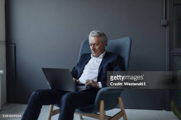 senior businessman sitting in armchair using laptop - man office chair stock pictures, royalty-free photos & images