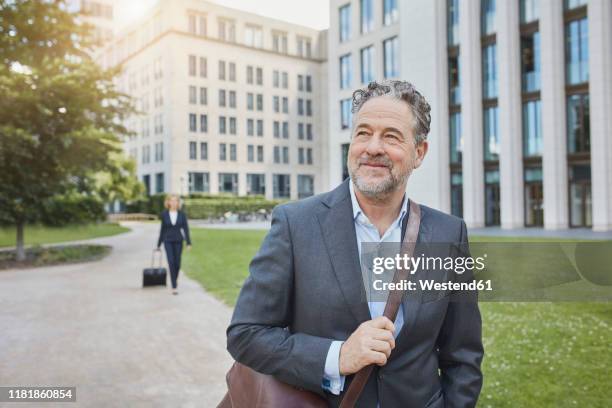 porrait of smiling businessman in the city with businesswoman in background - portrait man suit smiling light background stock pictures, royalty-free photos & images