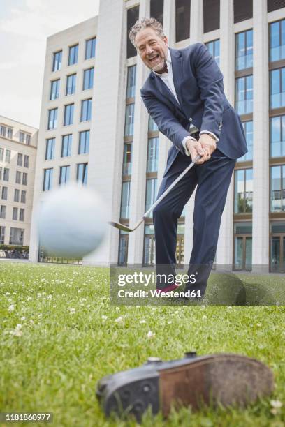 happy mature businessman playing golf on lawn in the city - playing golf stock-fotos und bilder