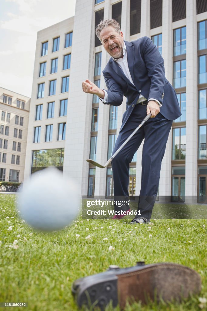 Happy mature businessman playing golf on lawn in the city