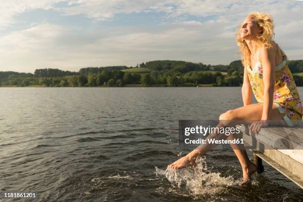 young woman sitting on a jetty at a lake with feet in water - jetty stock pictures, royalty-free photos & images