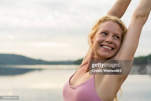 happy young woman raising her arms at a lake - alzar los brazos fotografías e imágenes de stock