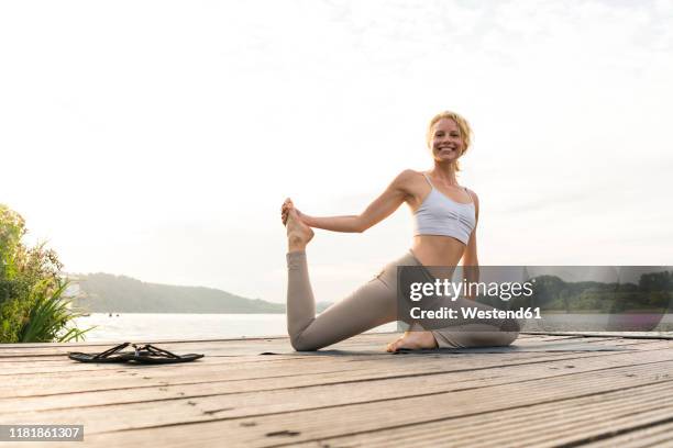 happy young woman doing gymnastics on a jetty at a lake - donne bionde scalze foto e immagini stock