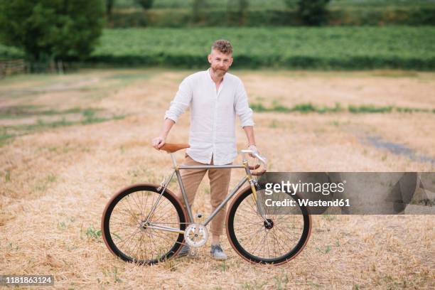 man with handcrafted racing cycle on stubble field - bartstoppel stock-fotos und bilder