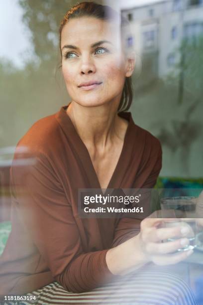 portrait of pensive woman with drink behind windowpane - behind window stock-fotos und bilder
