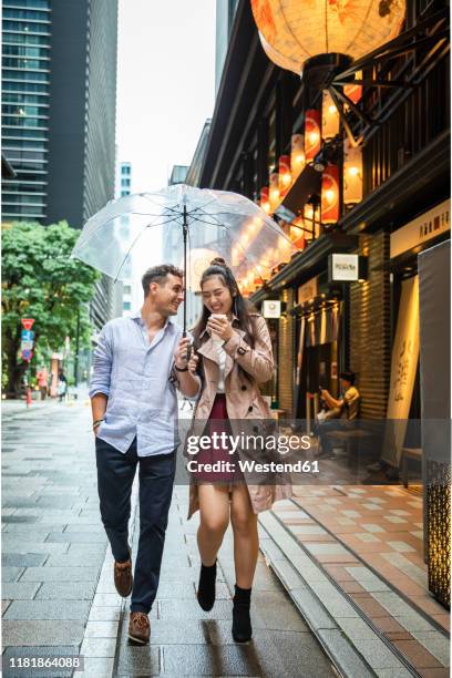 happy couple with umbrella walking in ginza, tokyo, japan - ginza stock pictures, royalty-free photos & images