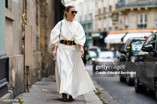 Guest wears sunglasses, a white pleated dress, a Valentino large belt with logo, outside Thom Browne, during Paris Fashion Week - Womenswear Spring...