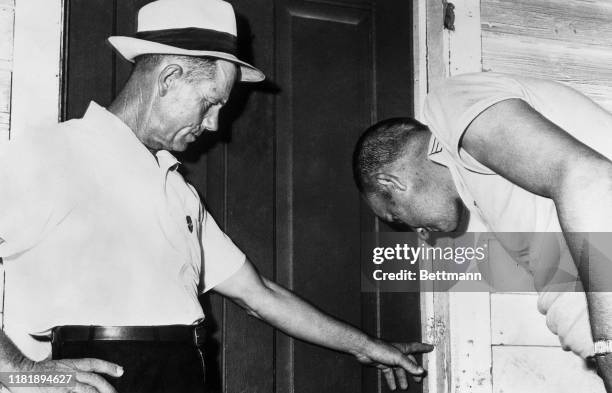 Sheriff's deputy Roy Carroll and Tom Griffin, who identified himself as a friend of slain Leroy Parks, inspect damage done by shotgun blast to door...