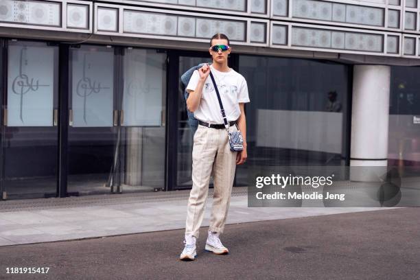 Model Kajus Valciukas wears reflective sunglasses, a white Dior t-shirt, Dior man bag, tan tweed pleated pants, and white Converse J.W. Anderson...