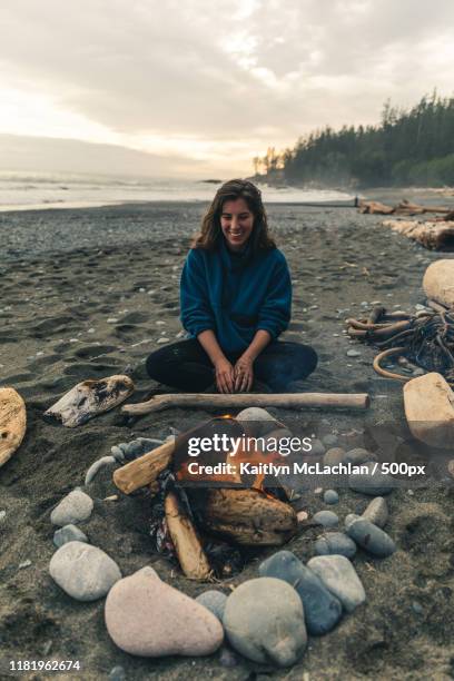 female sitting by beach campfire - canadian pacific women stock pictures, royalty-free photos & images