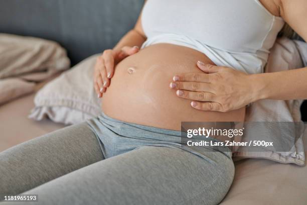 young pregnant woman rubbing moisturising cream on her belly - estrias fotografías e imágenes de stock