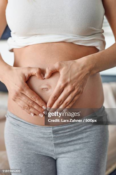 young pregnant woman making a heart gesture - belly button ストックフォトと画像