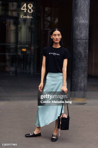 Model Lina Zhang wears a black Givenchy Paris shirt, teal asymmetrical silk skirt, black Givenchy bucket bag, and black Miu Miu ballerina flats after...